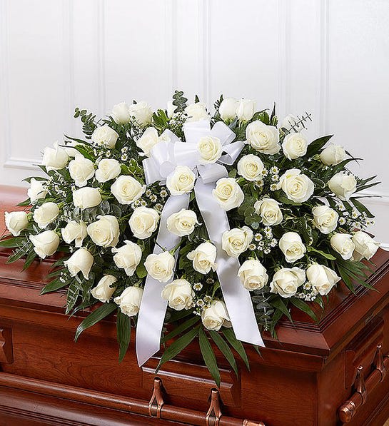 White rose casket spray with a white ribbon on a wooden coffin