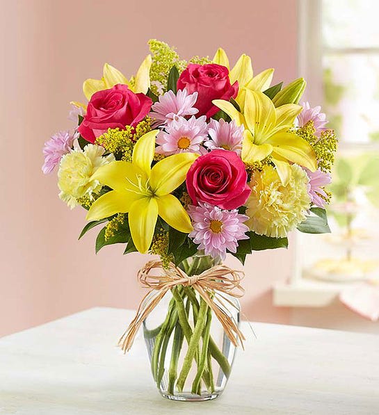 Bouquet of pink roses, yellow lilies, and daisies in a clear glass vase