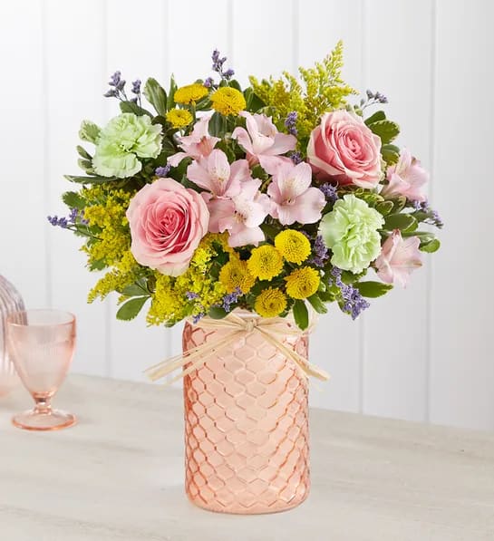 Pink roses and mixed flowers arranged in a peach glass vase