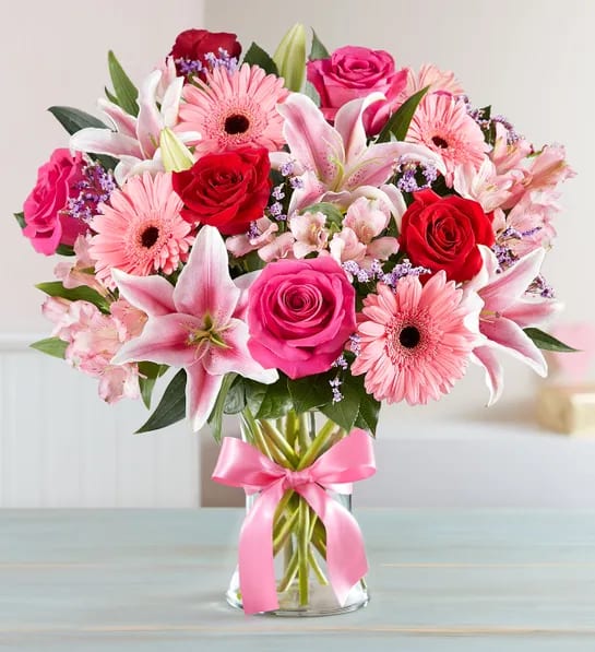 Pink and red bouquet of roses, lilies, and gerbera daisies in a glass vase