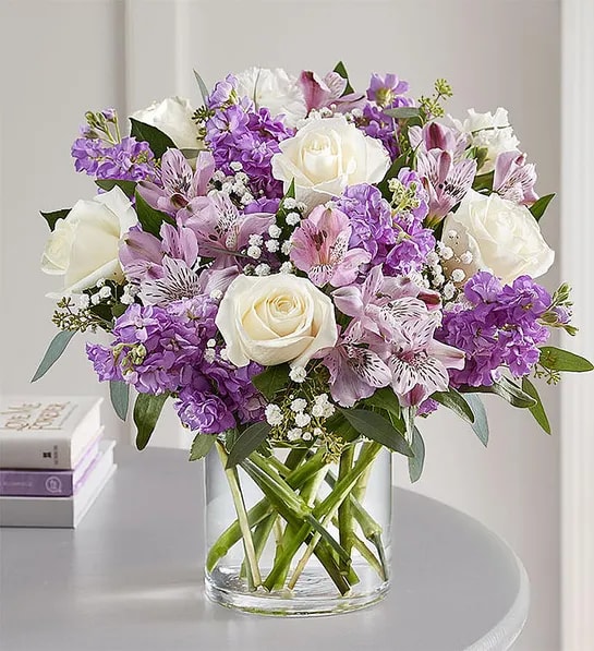 Bouquet of white roses and purple flowers in a clear glass vase