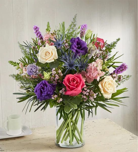 1800 Radiant Enchantment™ Bouquet - Our radiant arrangement is gathered with a unique variety of blooms in shades of purple, pink and cream. Lush greenery adds to its rich texture. Designed in a clear glass vase, it’s a luxurious gift to delight the people you love.  All-around arrangement with purple lisianthus and liatris, hot pink and cream roses, pink snapdragon and waxflower, blue thistle; accented with assorted, unique greenery Artistically designed in a clear glass cylinder vase; measures 8"H Large arrangement measures approximately 27"H x 24"W Medium arrangement measures approximately 24"H x 21"W Small arrangement measures approximately 23"H x 20"W Our florists hand-design each arrangement, so colors, varieties and container may vary due to local availability