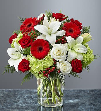 Garden of Grandeur Holiday - Product ID: 99143 Celebrate love and sophistication with this stunning bouquet of red roses, white lilies, and vibrant red gerbera daisies, accented by lush greenery and seasonal berries. Designed in a clear glass vase, this premium floral arrangement is perfect for Valentine’s Day romance, Mother’s Day admiration, or any occasion that calls for elegance and beauty. A timeless gift that speaks the language of love.