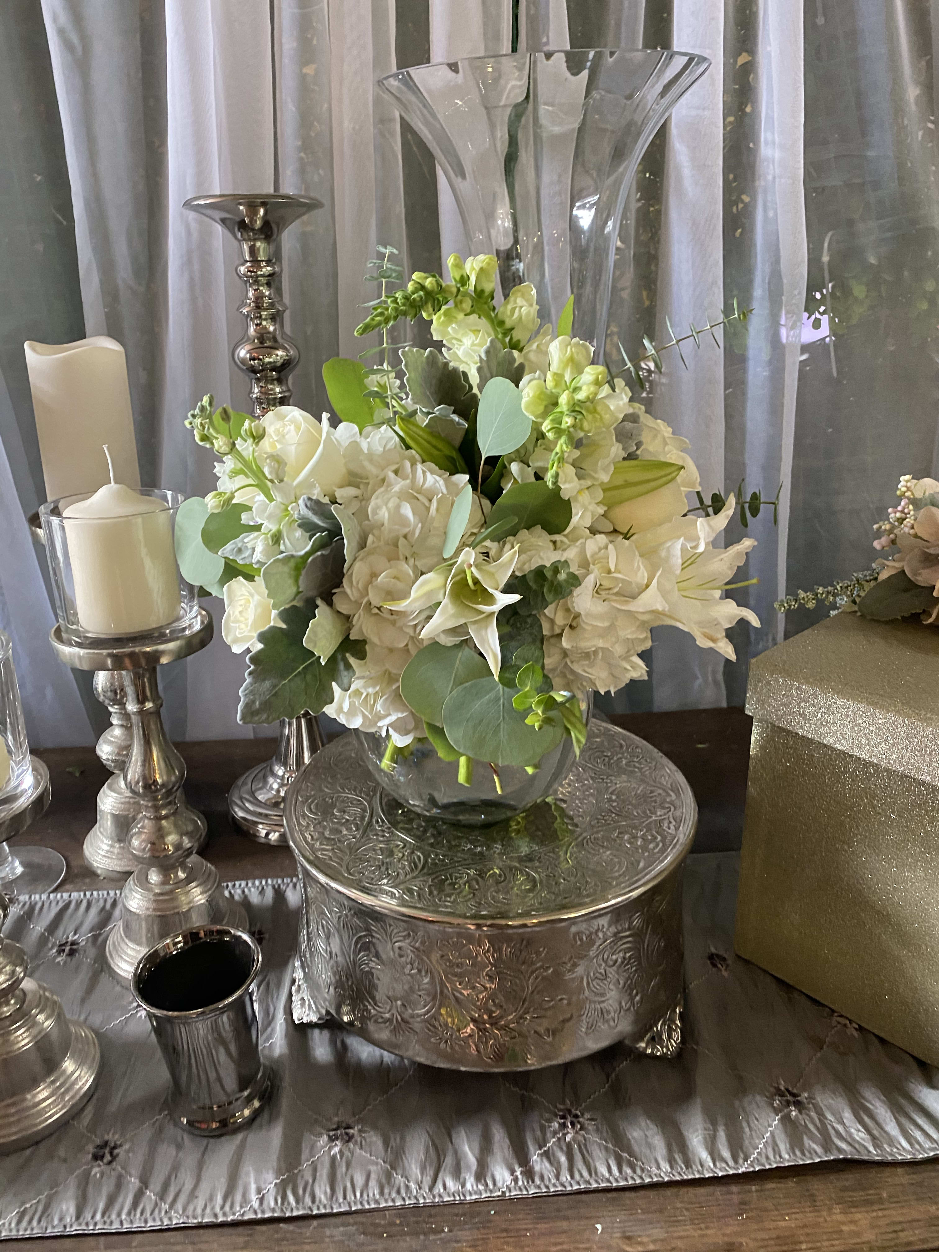 White floral centerpiece in a glass vase on a silver stand