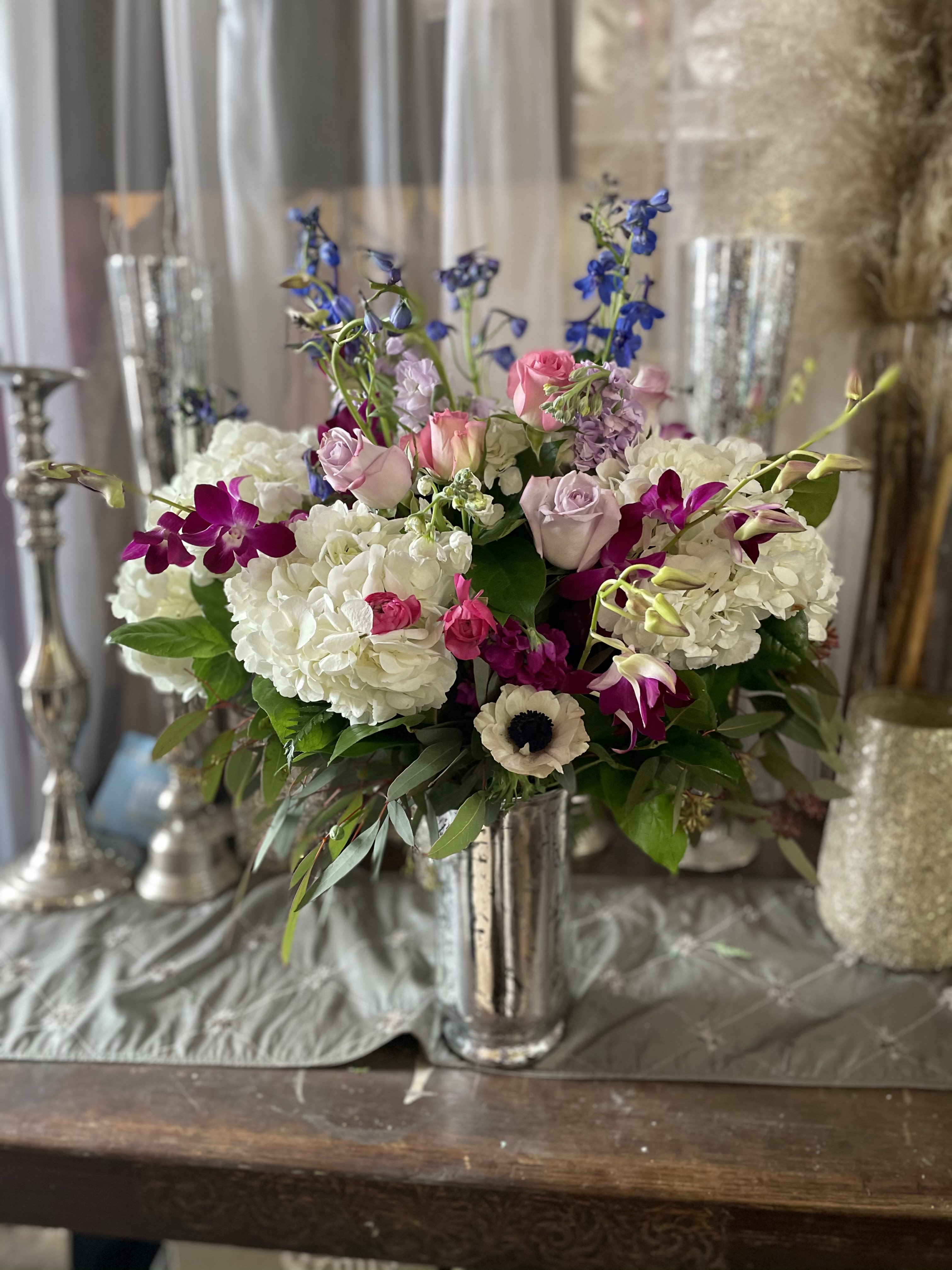 Mixed bouquet of white hydrangeas, pink roses, and purple orchids in a silver vase