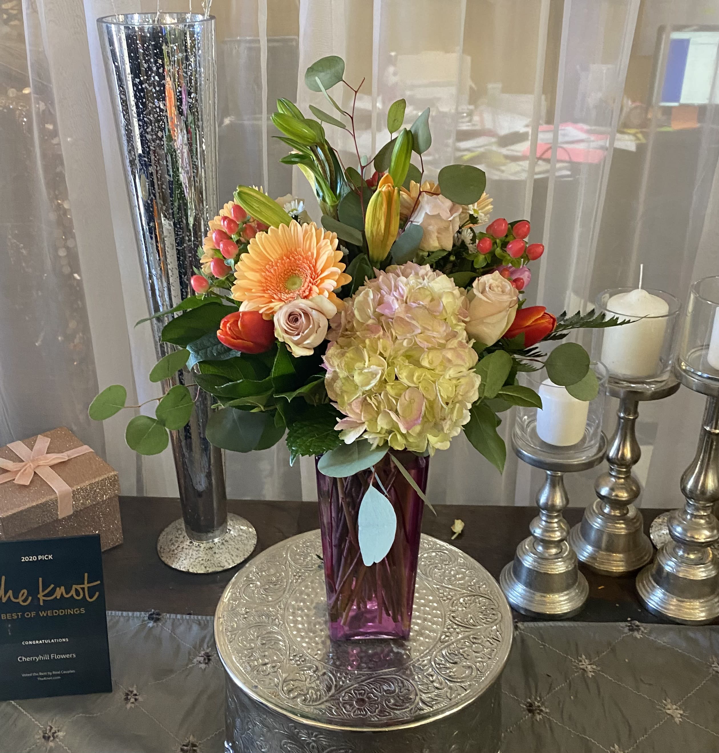 Mixed bouquet in a purple vase with candles and a gift box nearby