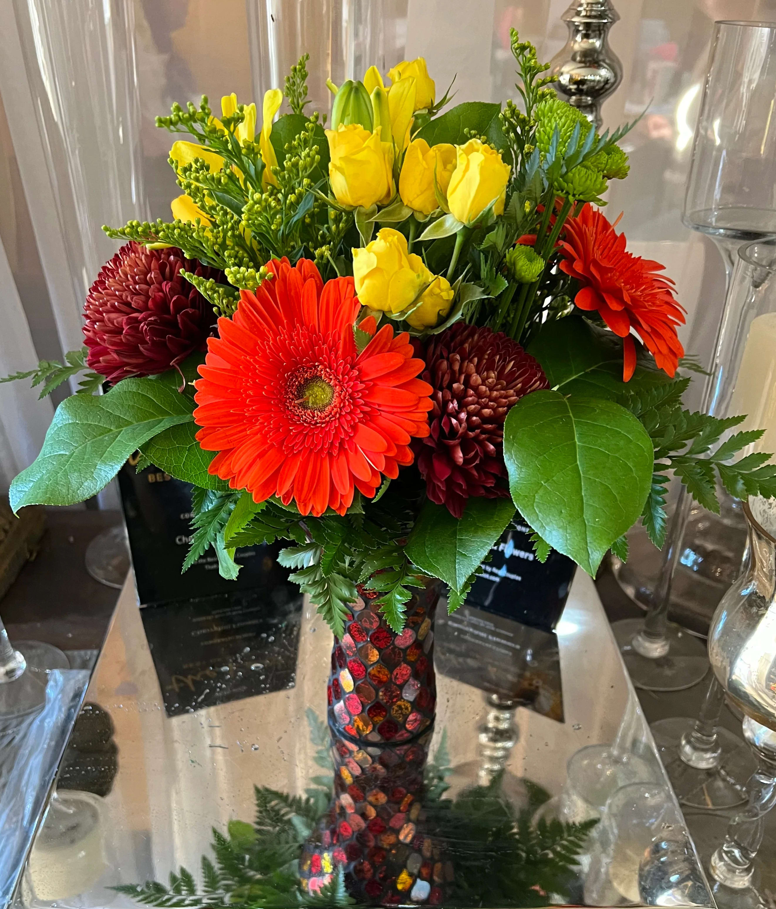 Bright bouquet of yellow roses and red gerbera daisies in a mosaic vase