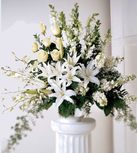 White lilies and pale yellow roses in a white pedestal vase