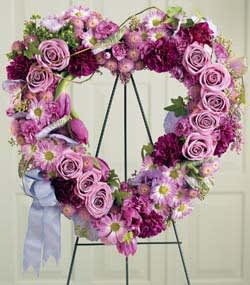 Heart-shaped floral wreath with pink roses and daisies on a stand