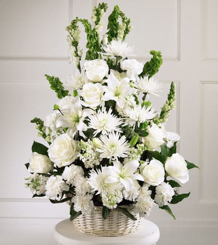 White floral arrangement in a wicker basket with roses, lilies, and spiky blooms