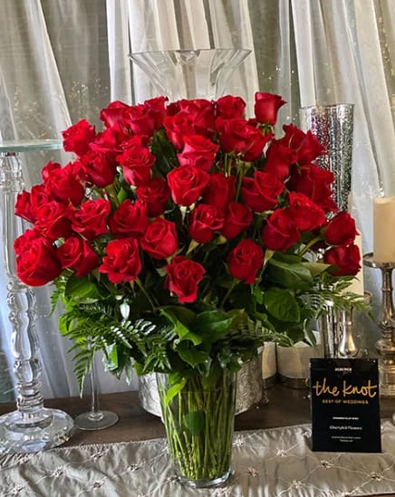 Tall vase arrangement of red roses with greenery