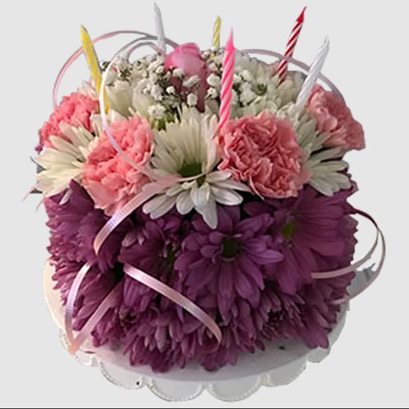 Pink and purple flower arrangement with striped candles in a white container