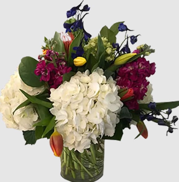 Mixed bouquet with white hydrangeas, purple blooms, and tulips in a glass vase