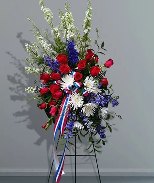 Standing floral spray with red roses, white daisies, and blue flowers on an easel