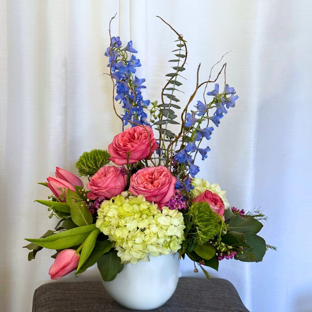 Pink roses and tulips with blue delphinium in a white vase