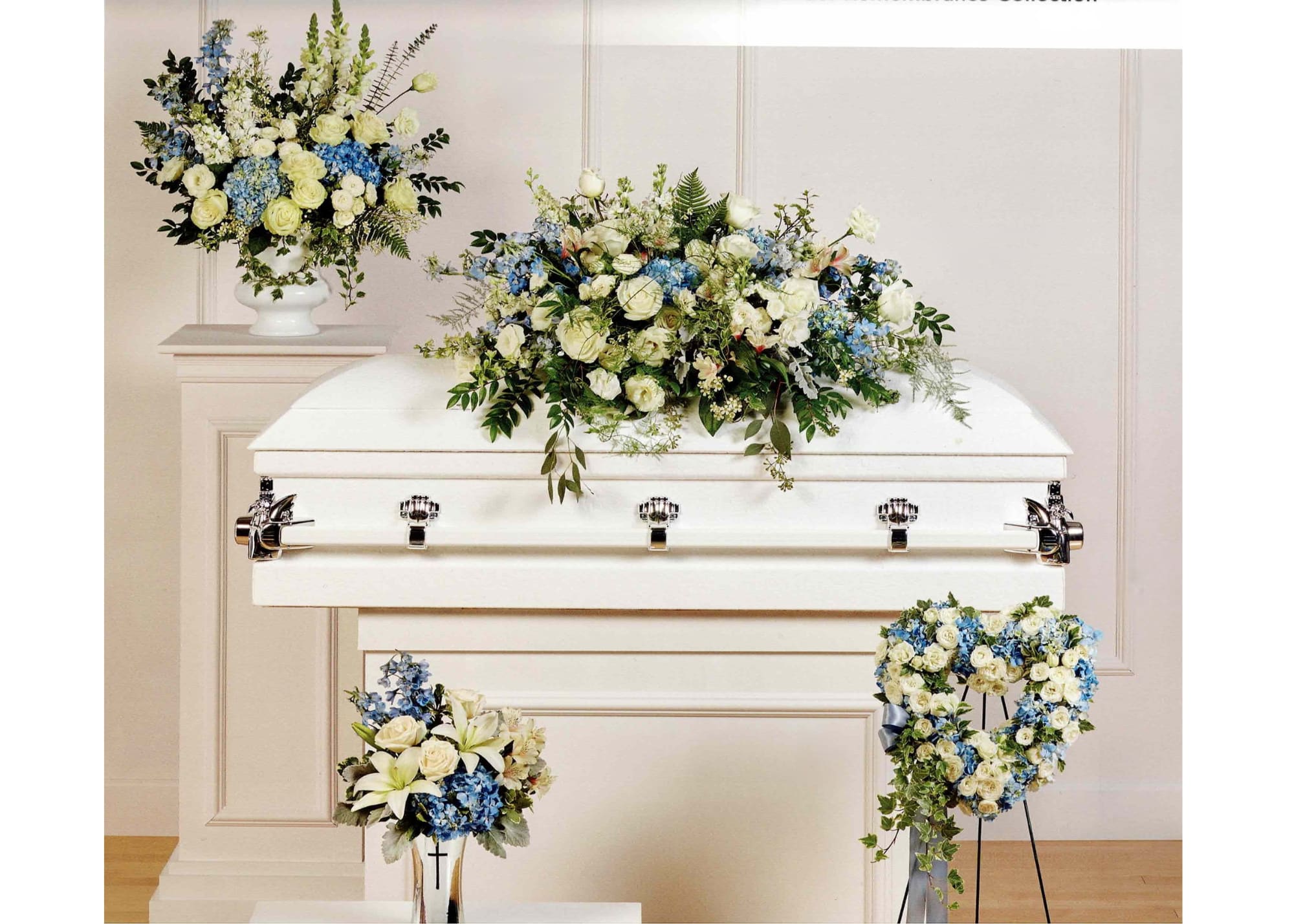 White casket with blue and cream floral sprays and arrangements