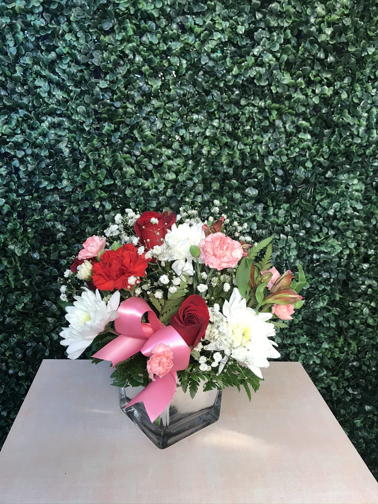 Bouquet of red, pink, and white flowers in a glass vase with a pink ribbon