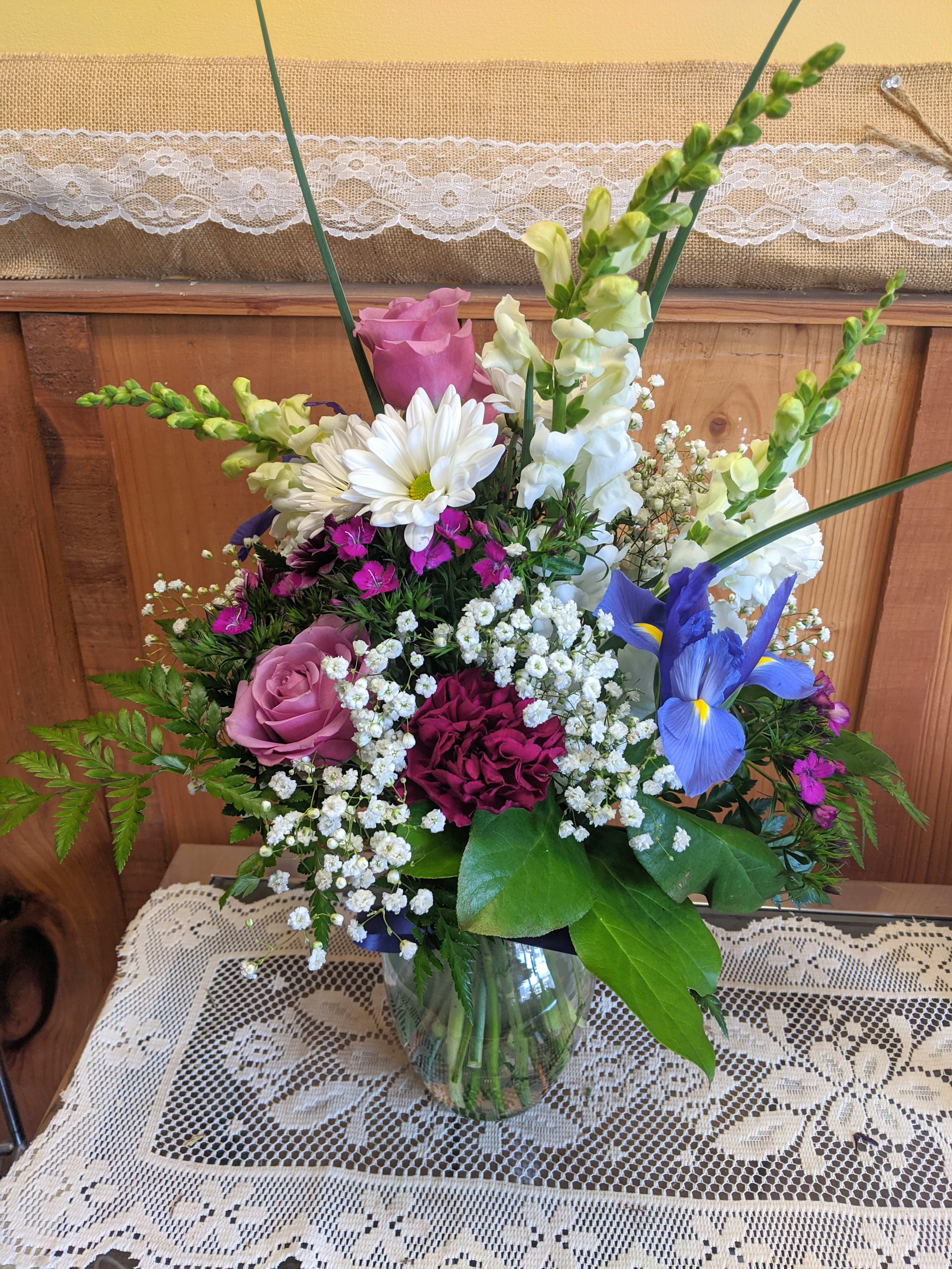 Mixed bouquet in a glass vase with roses, daisies, iris, and snapdragons