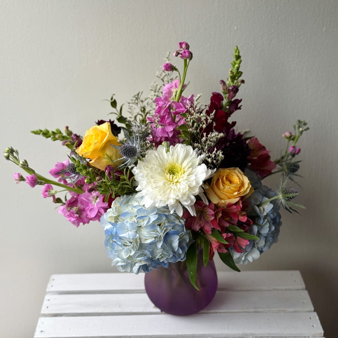 Mixed bouquet in a purple vase with roses, hydrangeas, and a white chrysanthemum