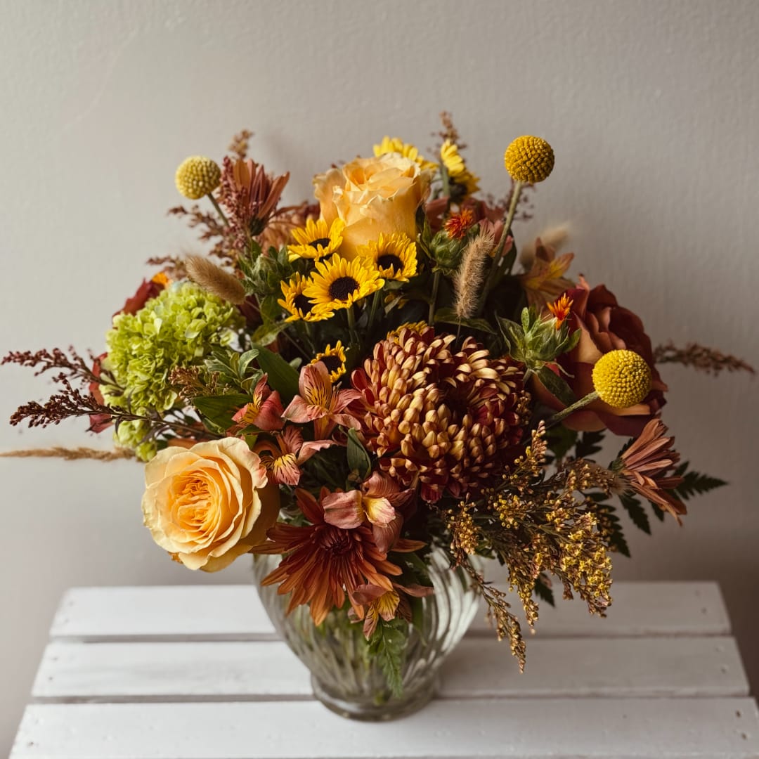 Autumn bouquet of roses, chrysanthemums, and yellow accent blooms in a glass vase