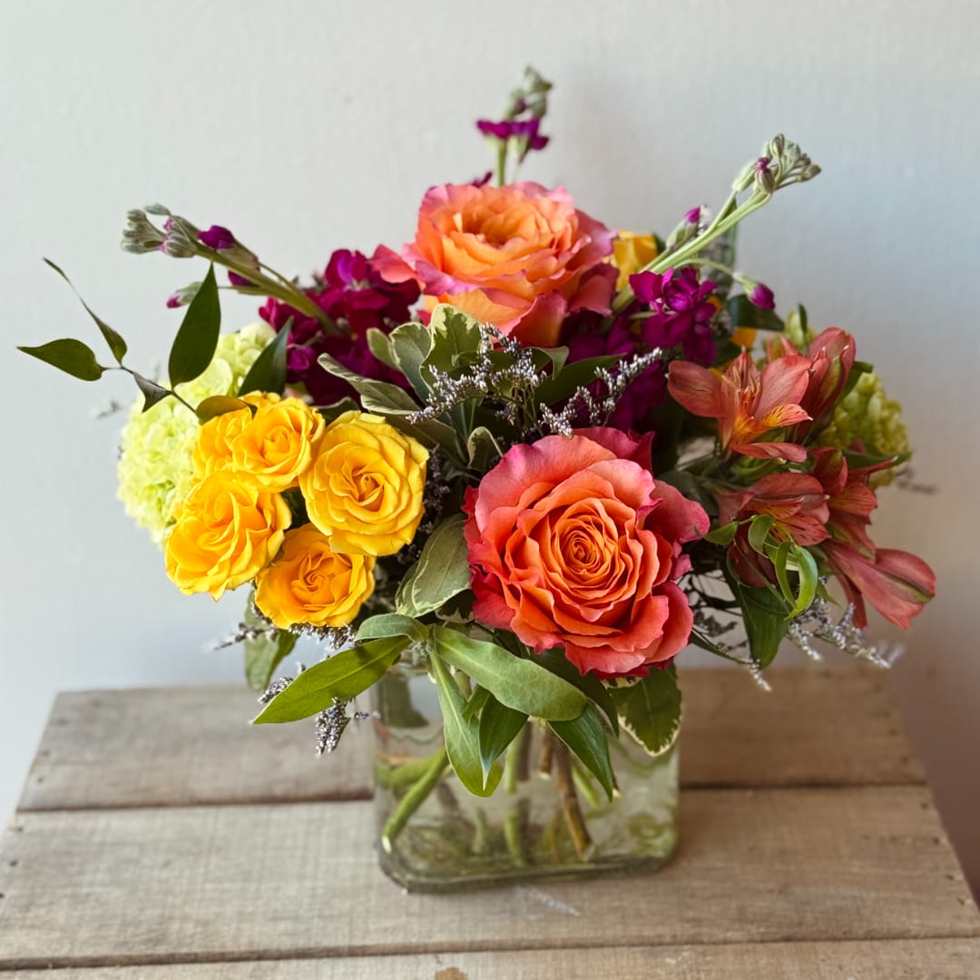 Mixed bouquet of orange, yellow, and pink flowers in a glass vase