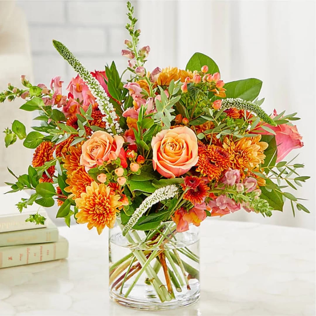 Peach roses and orange chrysanthemums in a clear glass vase