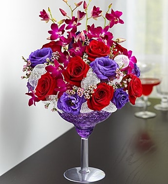 A Toast to Love - Product ID: 105225  EXCLUSIVE Stir up something truly originalâand truly romanticâfor someone close to your heart. Our fresh floral cocktail is hand-arranged in a keepsake margarita glass with a mixture of red roses, purple orchids, lisianthus and waxflower. Without a doubt, itâs the perfect romantic recipe for first dates, anniversaries or just because their smile is intoxicating! Cocktail-shaped floral arrangement of red roses, purple Dendrobium orchids, purple lisianthus and pink waxflower, accented throughout with white poly mesh for a contemporary look Artistically designed by our florists in a 10"H reusable acrylic margarita glass filled with purple crystal gel Extra large arrangement measures approximately 14.5"H x 7.5"L Large arrangement measures approximately 14"H x 7"L Medium arrangement measures approximately 13.5"H x 6.5"L Small arrangement does not include orchids and measures approximately 13"H x 6"L Our florists select the freshest flowers available so colors and varieties may vary