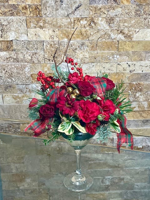 Red floral arrangement in a wine glass vase with plaid ribbon