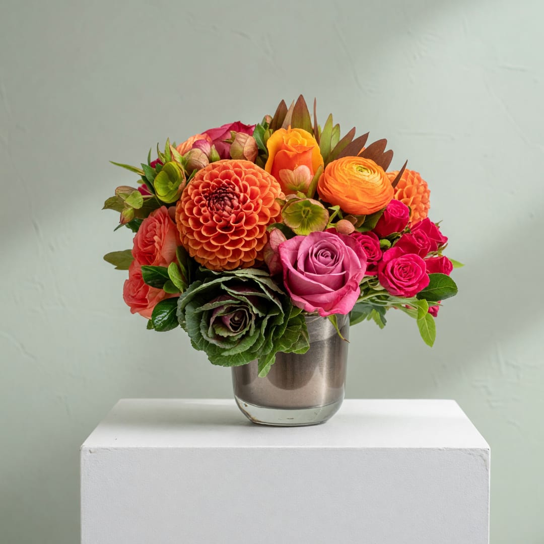 Mixed bouquet of orange, pink, and red flowers in a glass vase