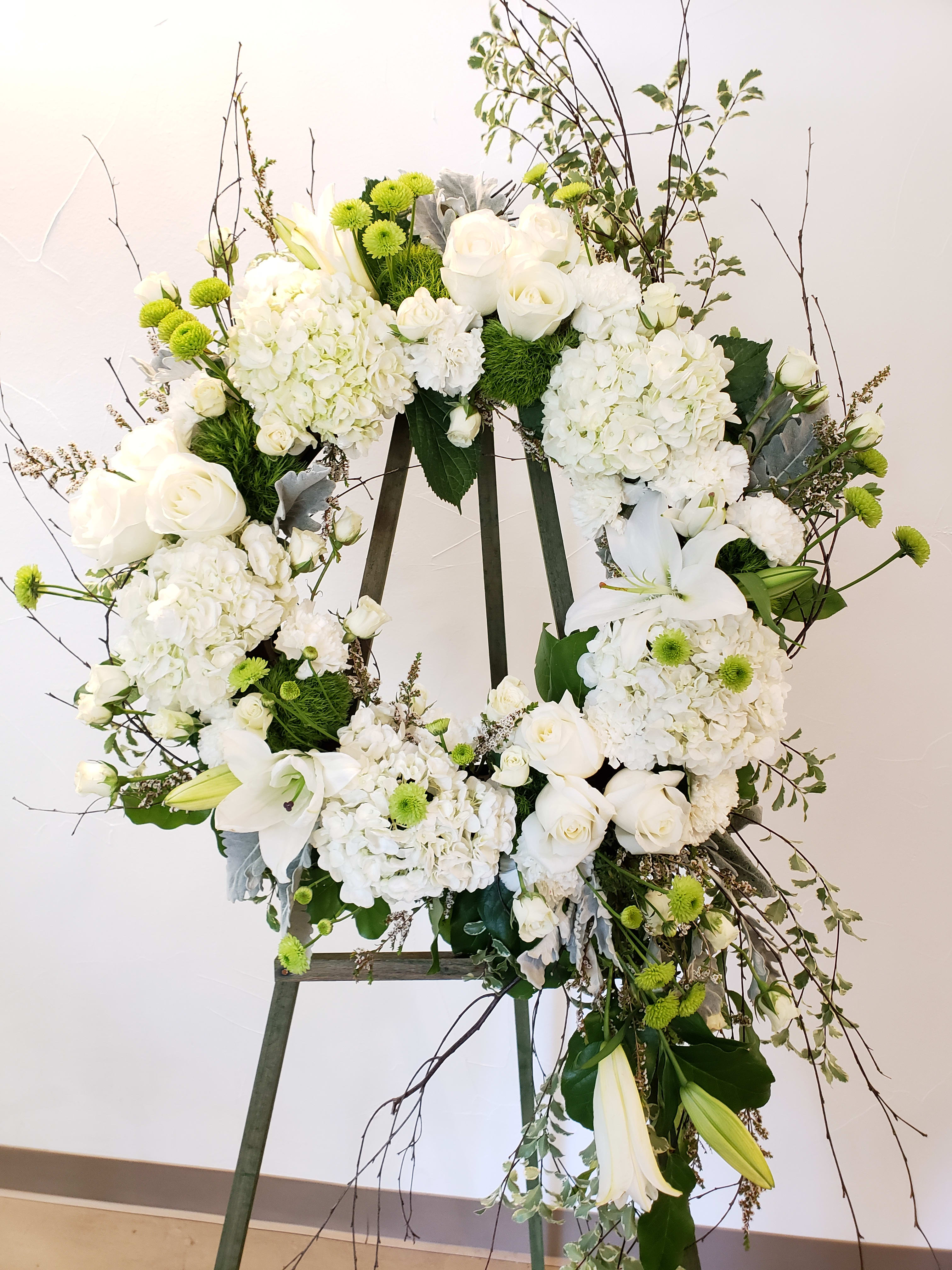 White floral wreath on an easel with roses and lilies