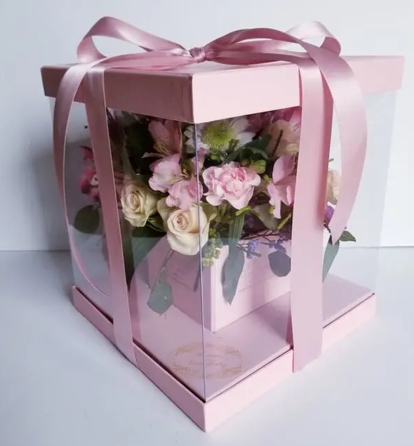 Pink roses and carnations in a clear gift box with a ribbon bow