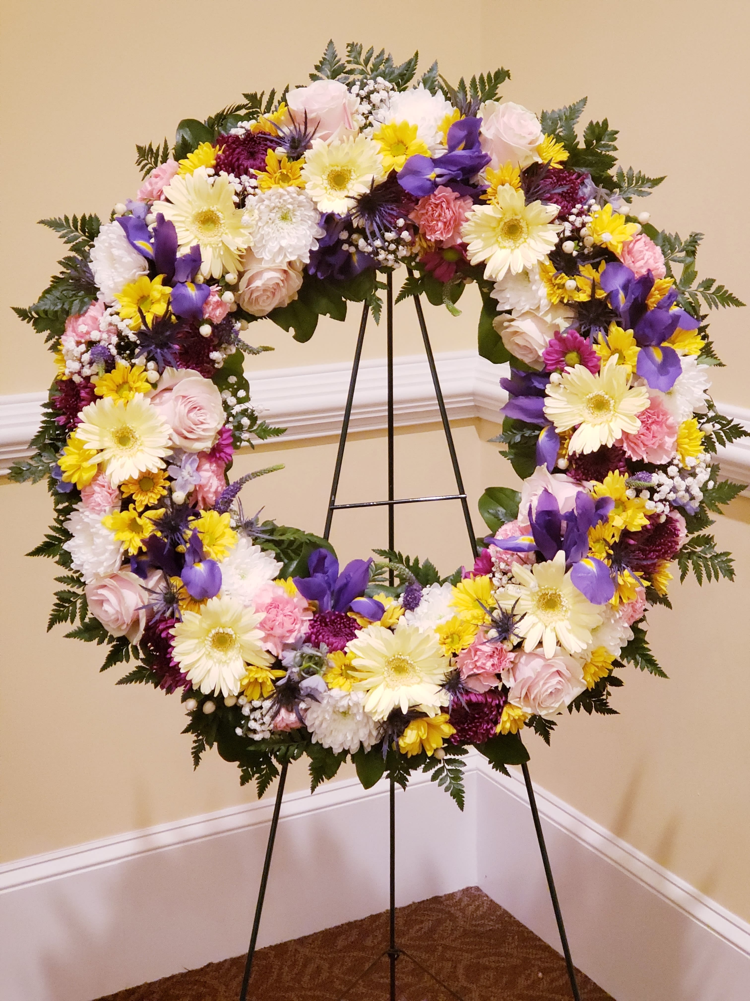 Warm Thoughts Wreath - A bright standing wreath of greenery and fresh flowers in yellow, pink, blue and white will send a message of hope and harmony, and help to celebrate a meaningful life. If you would like different color or flowers of wreath please contact us.