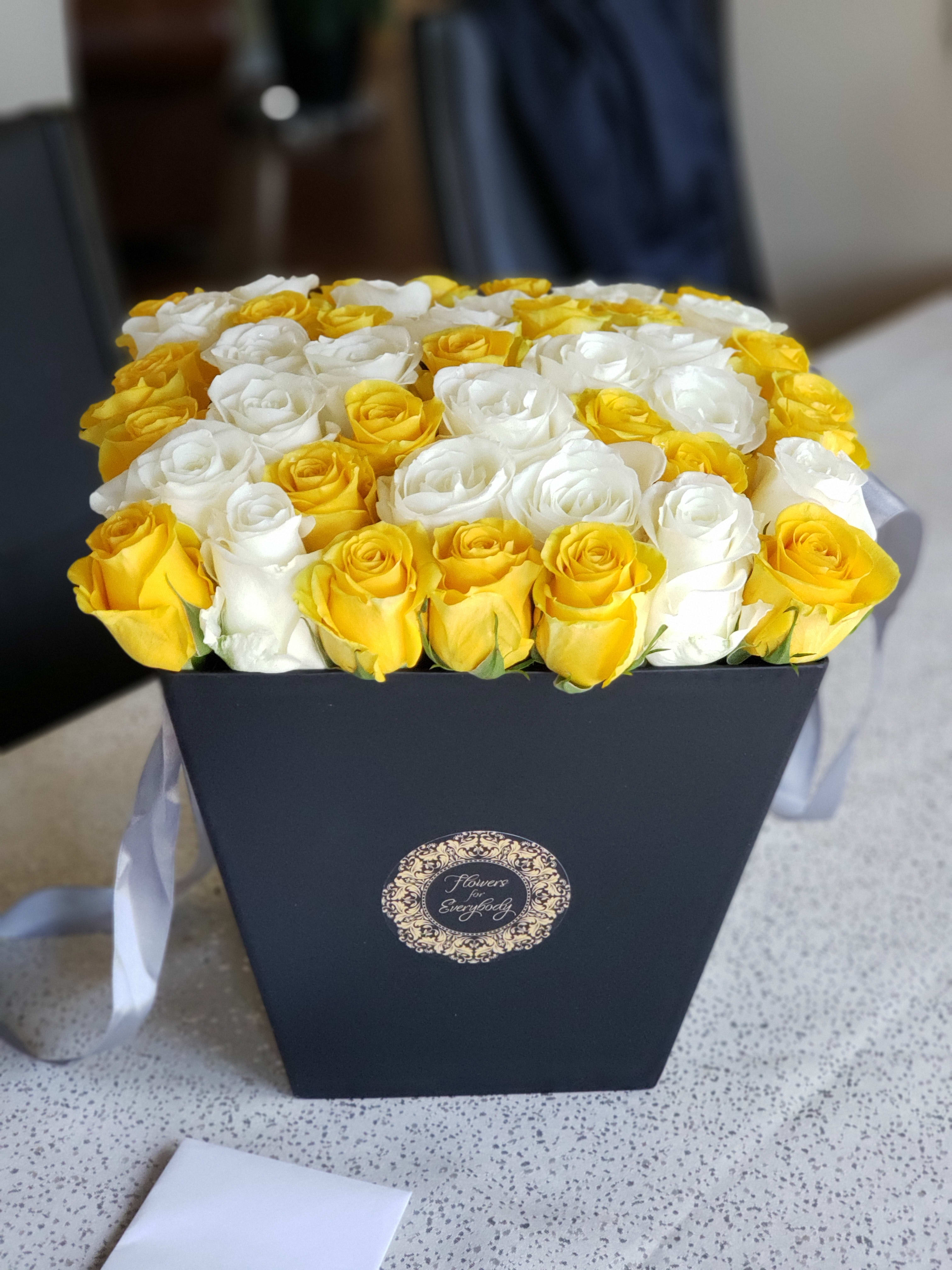 Yellow and white roses arranged in a black box with a ribbon