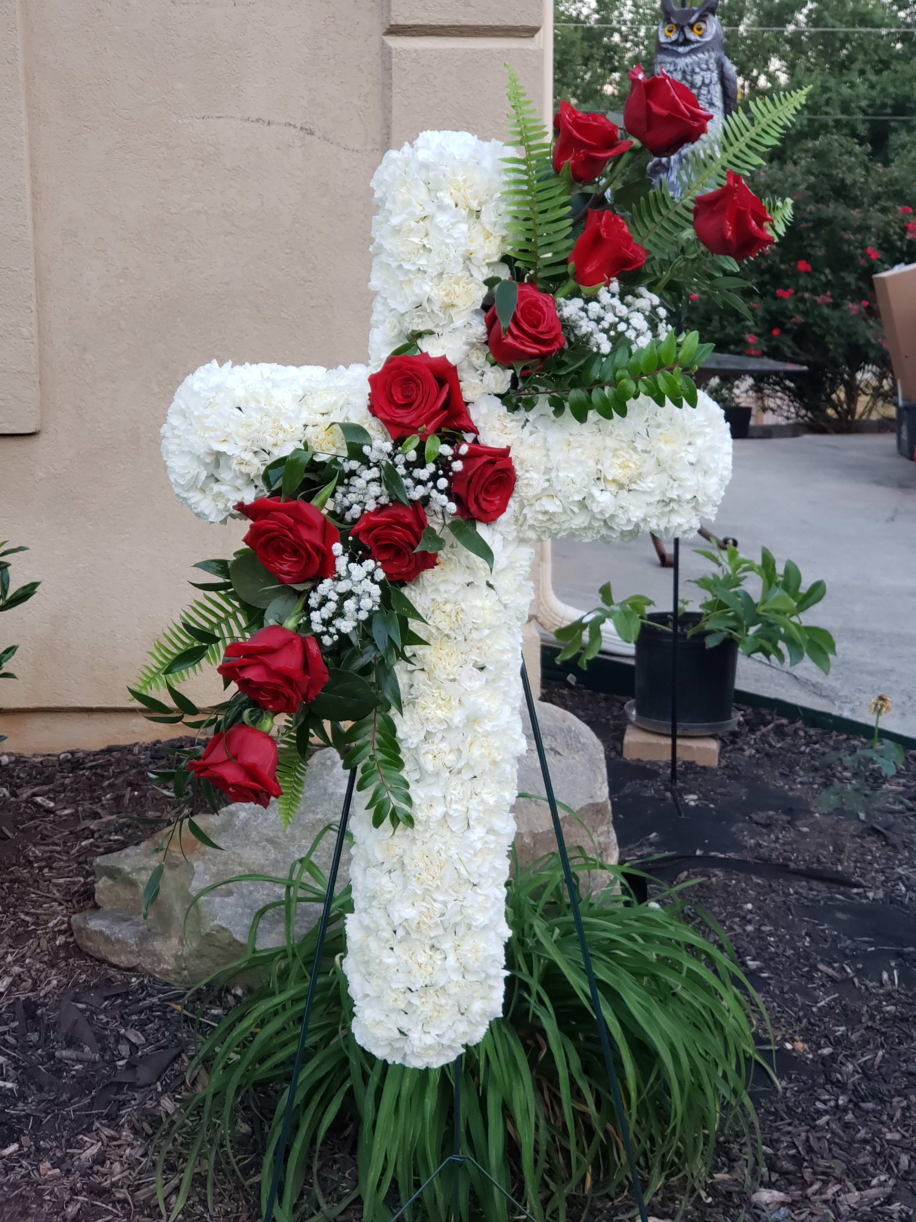 White Cross Standing Spray - Standing spray cross of white blossoms (carnations) adorned with red roses. It’s a display that remembers faith, hope and charity. 