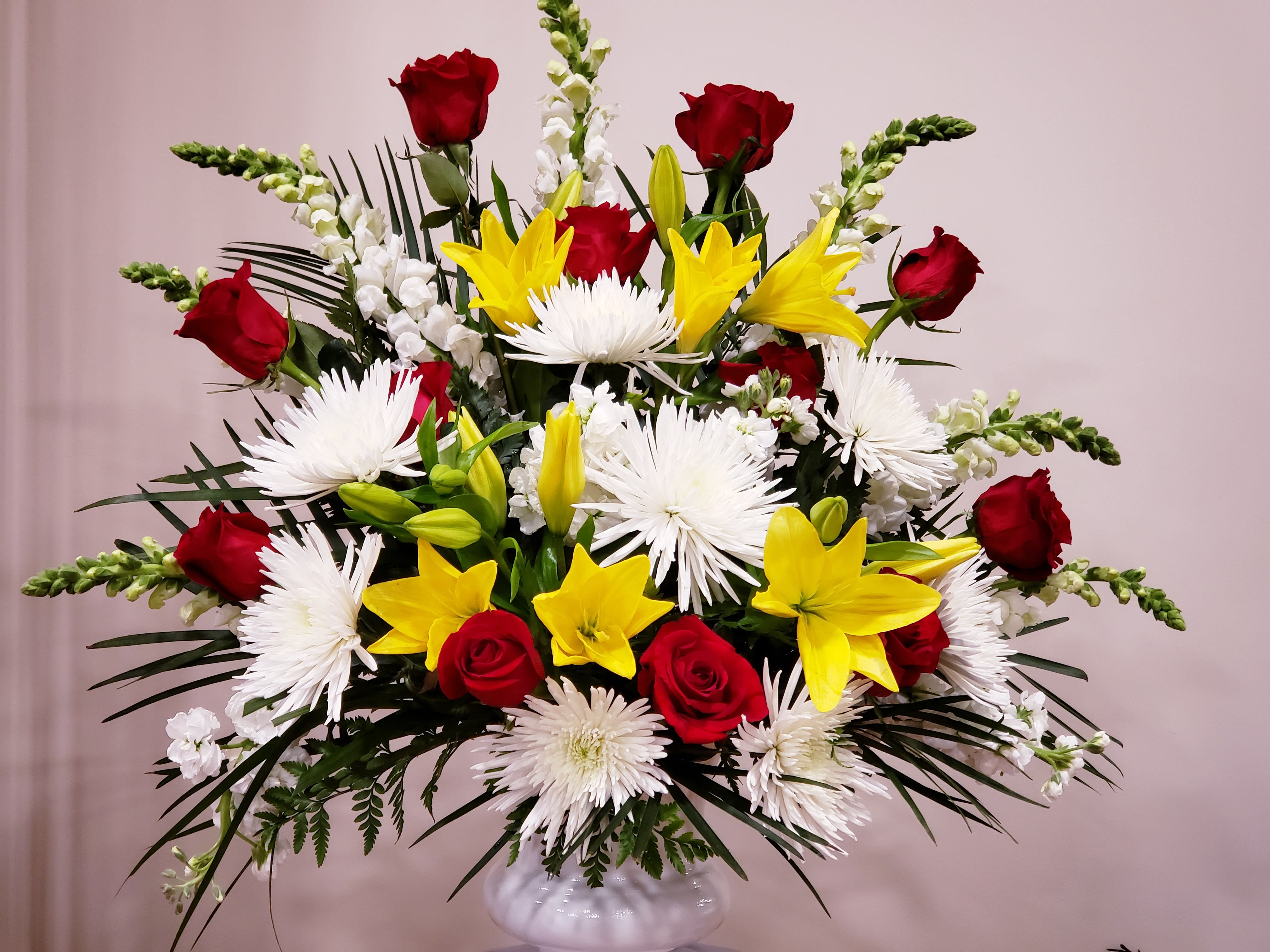 Large bouquet of red roses, yellow lilies, and white spider mums in a white vase