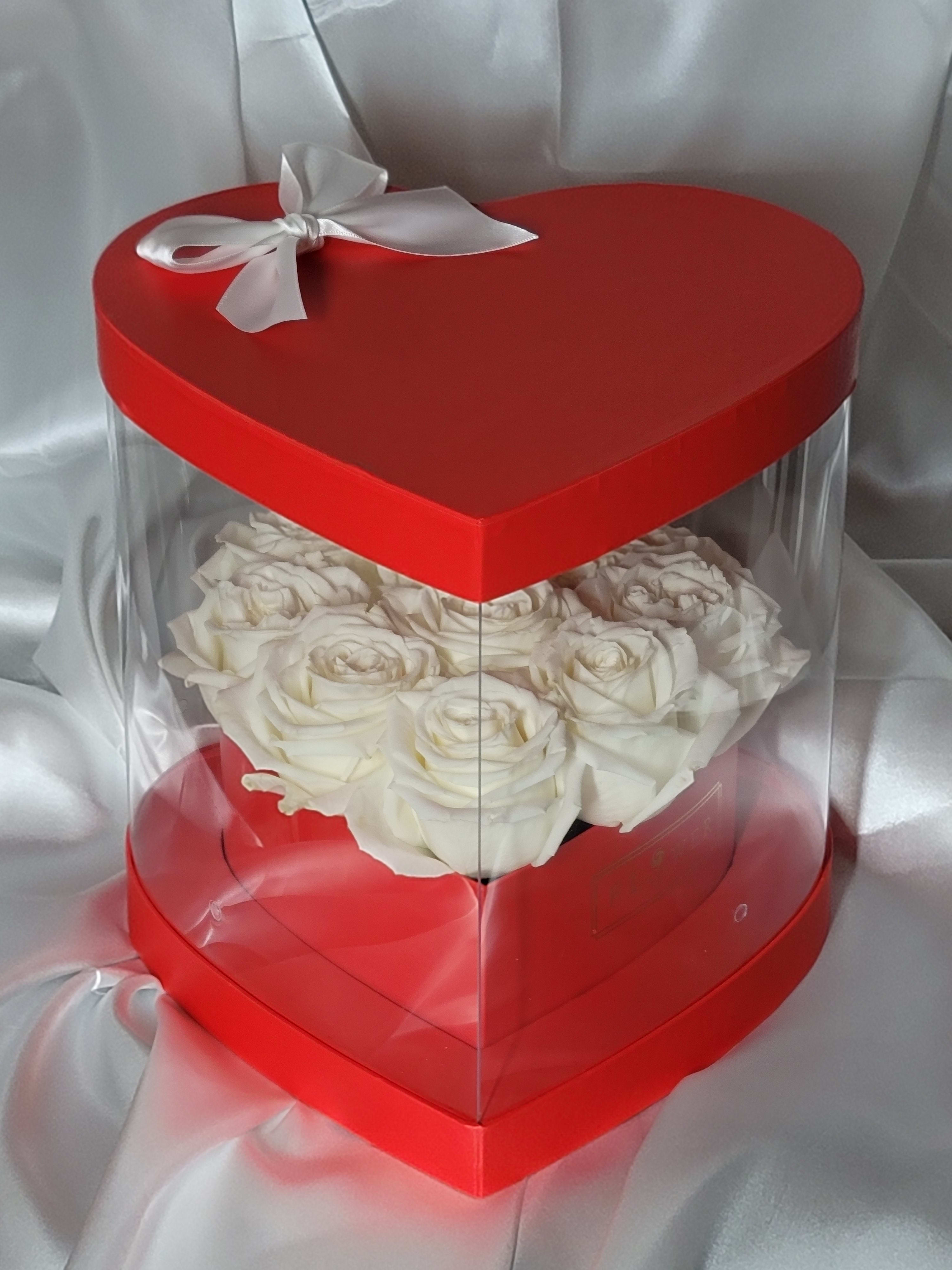 White roses in a red heart-shaped gift box with a clear cover and white ribbon