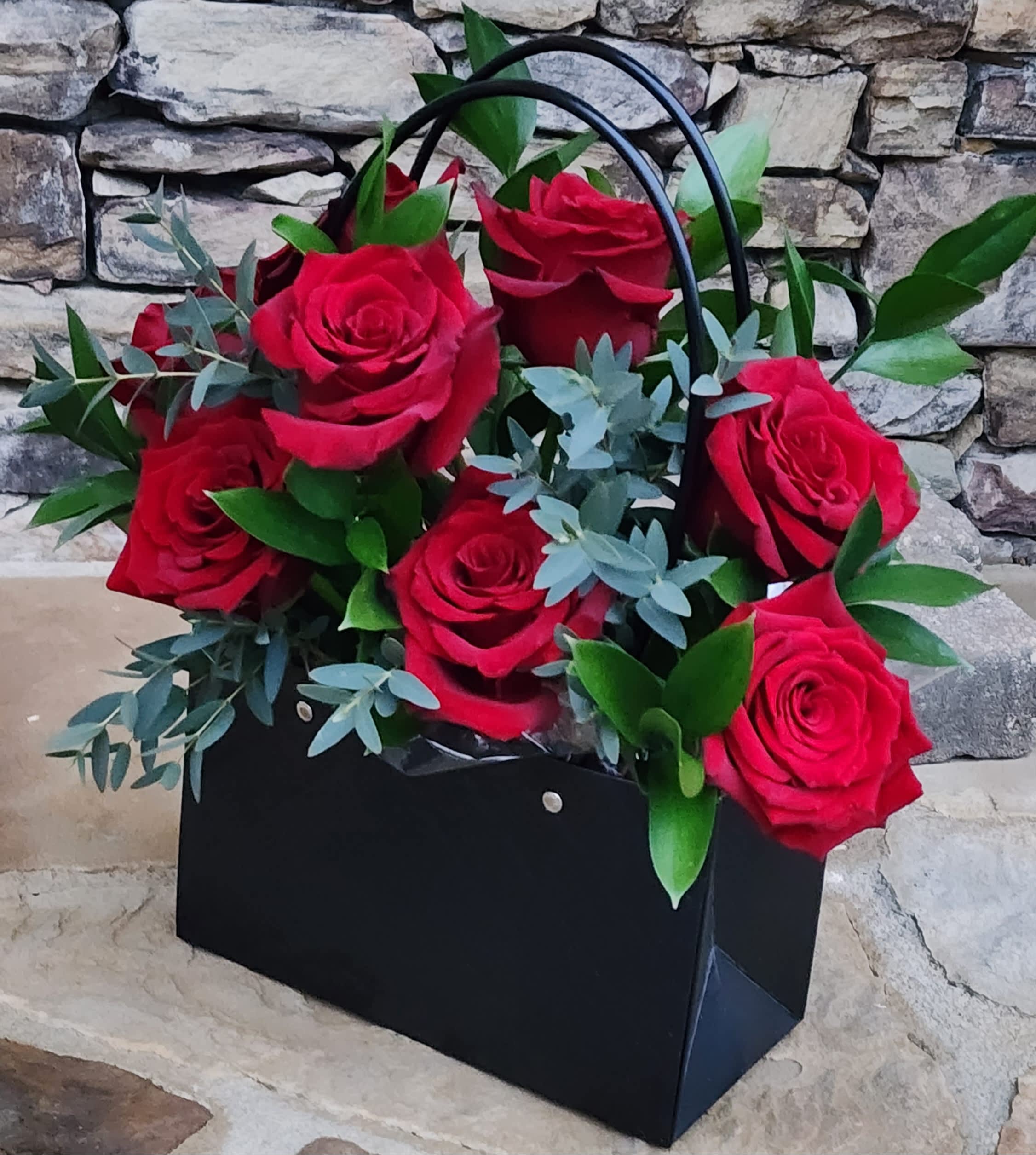 Black gift bag filled with red roses and greenery