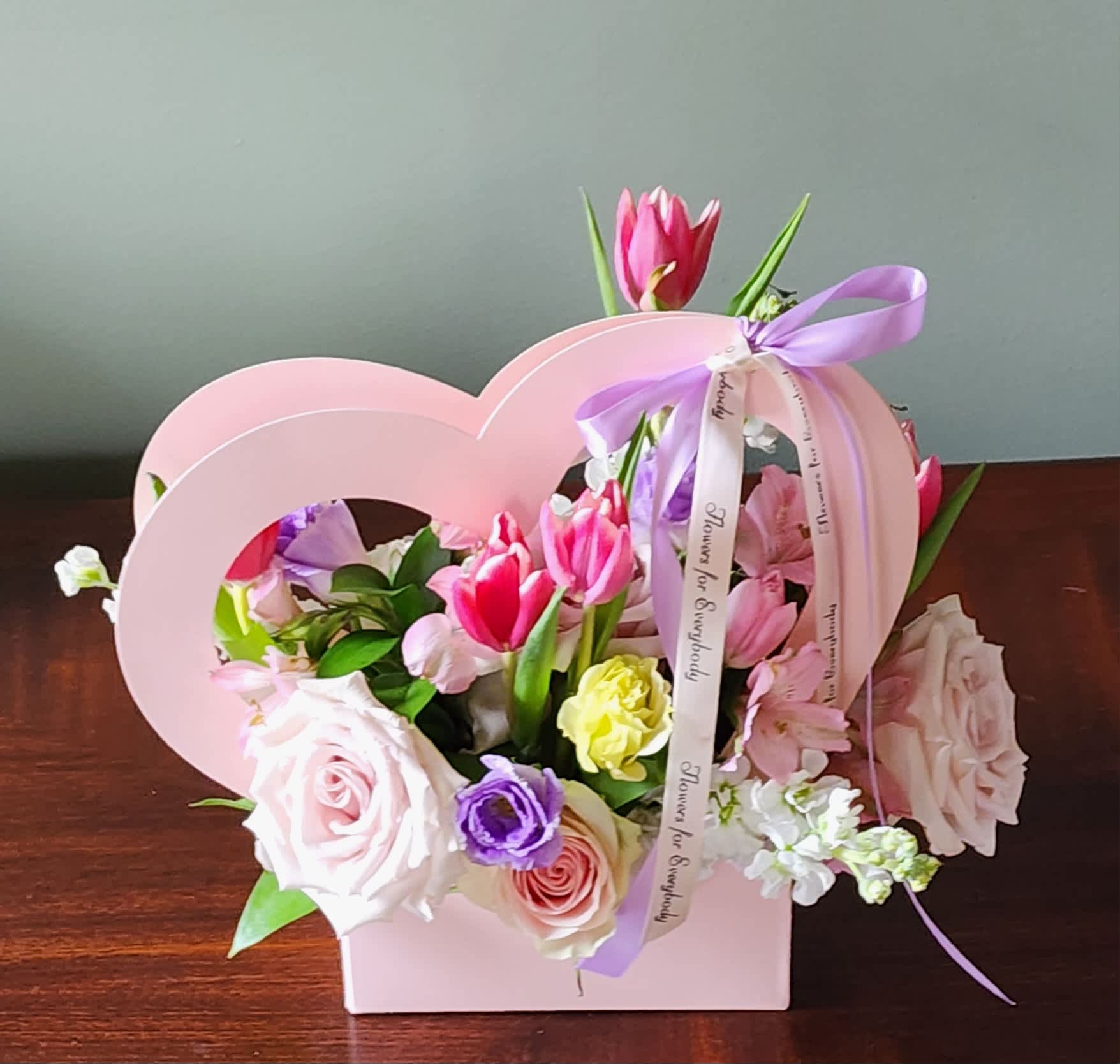 Pink and purple flower arrangement in a heart-shaped box with ribbon