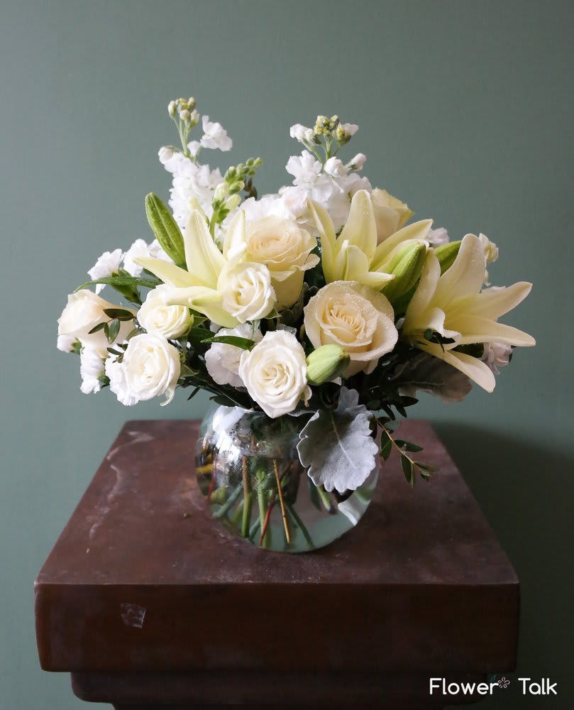 White lilies and roses arranged in a round glass vase