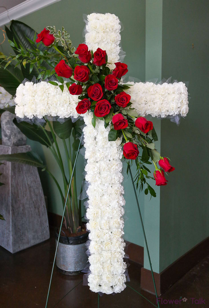 White floral cross with red roses on a stand