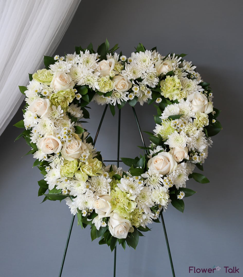 Heart-shaped floral wreath with white roses and chrysanthemums on a stand