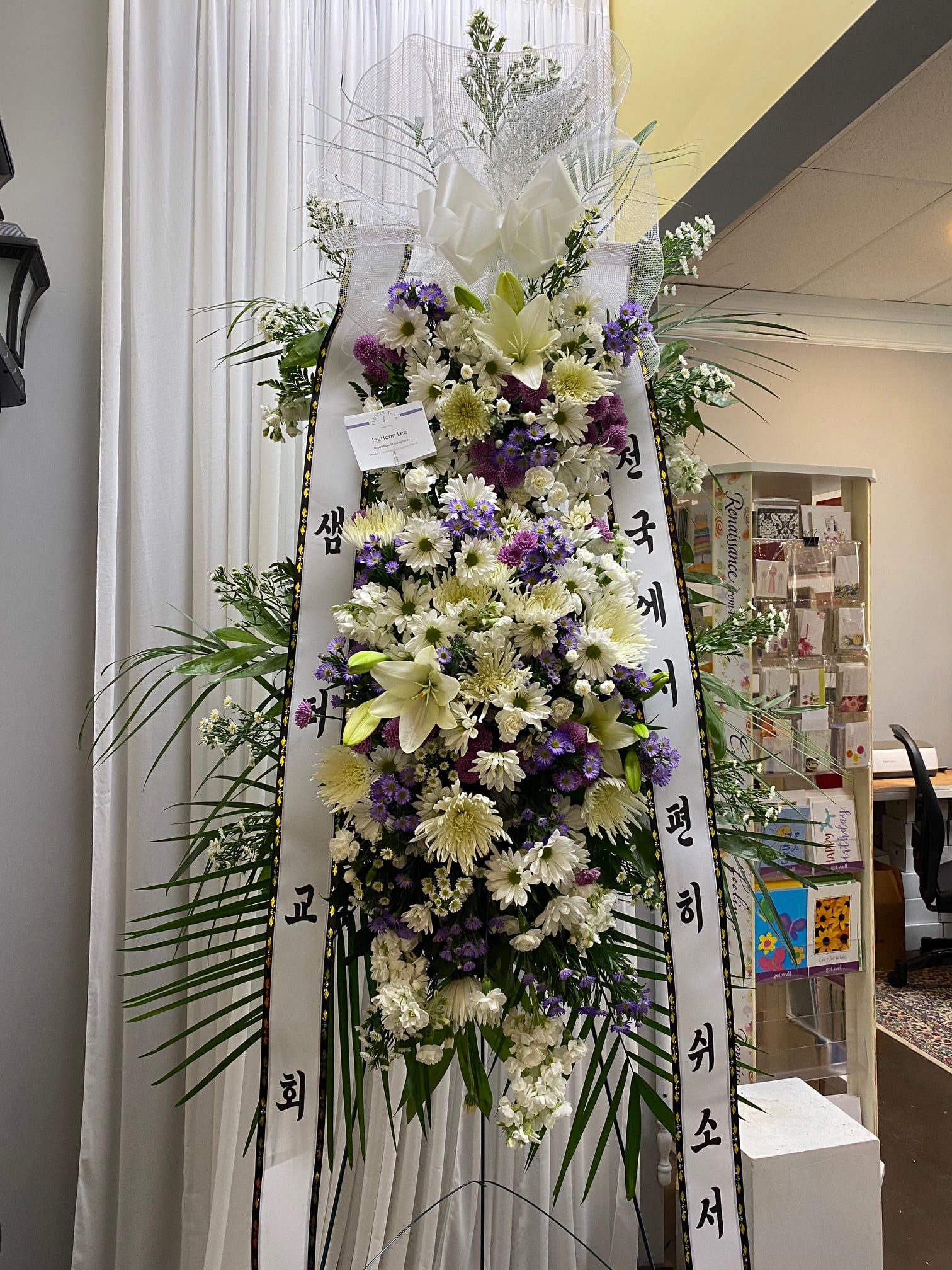 Tall standing floral wreath with white and purple flowers and ribbon streamers