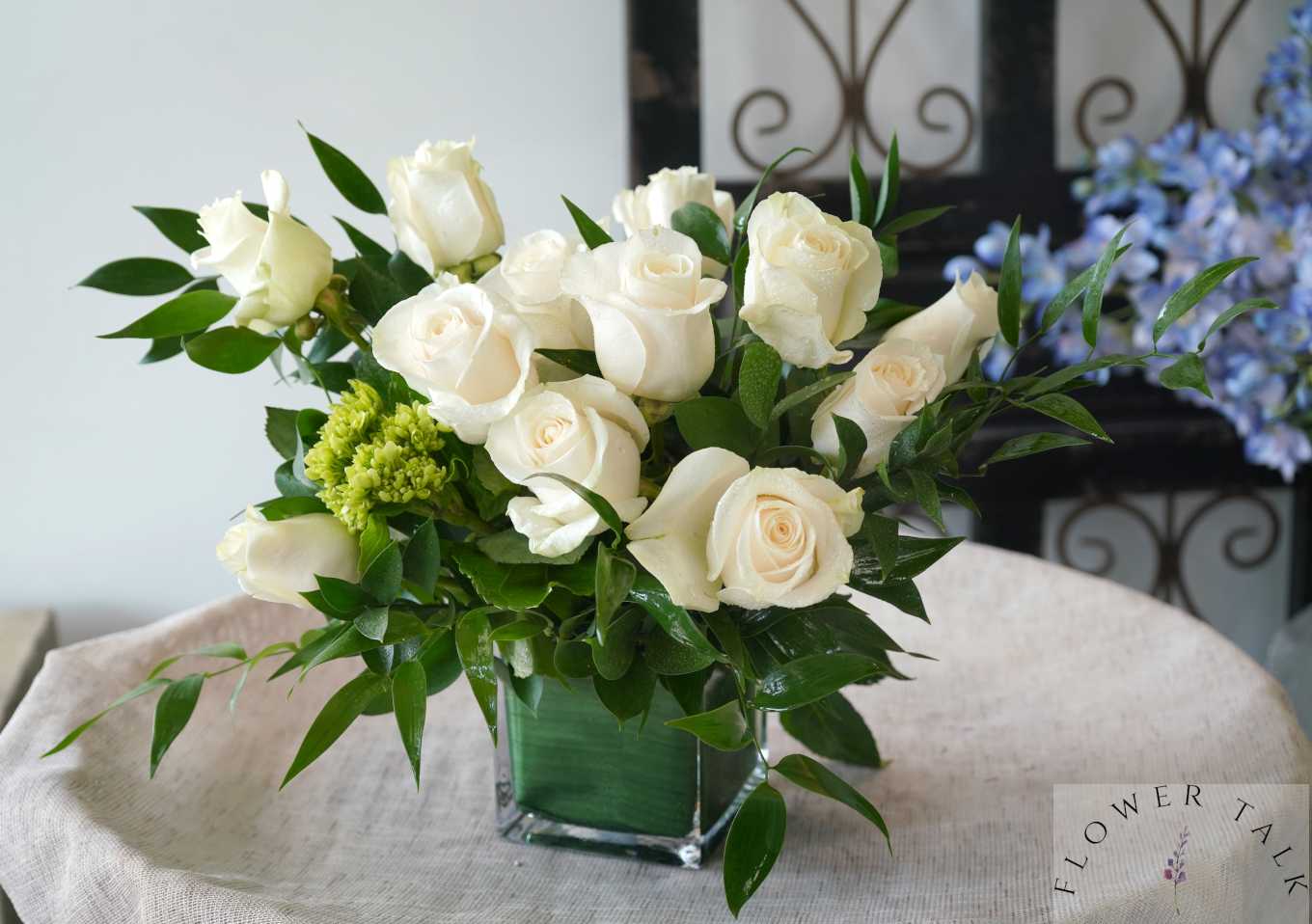 White roses arranged in a square glass vase with green foliage
