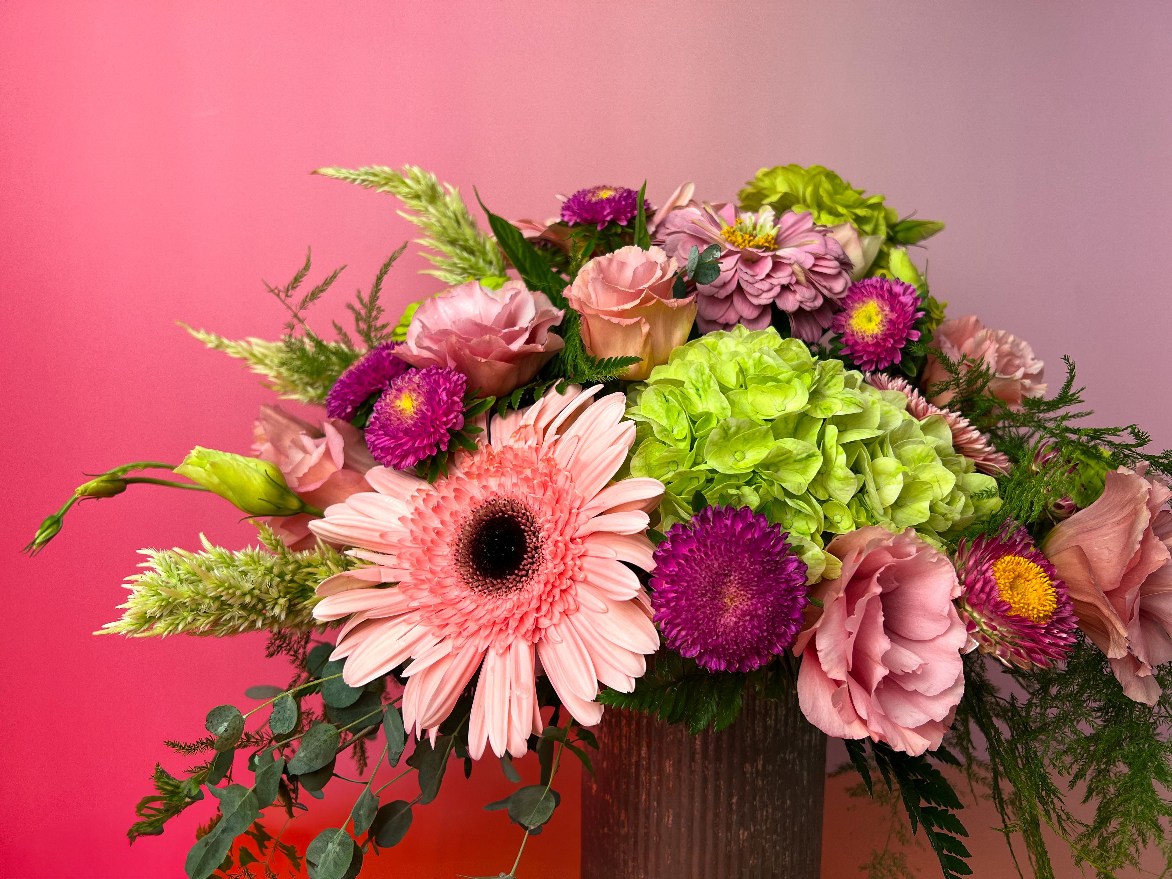 Pink and purple mixed flower arrangement in a vase with a bright green hydrangea