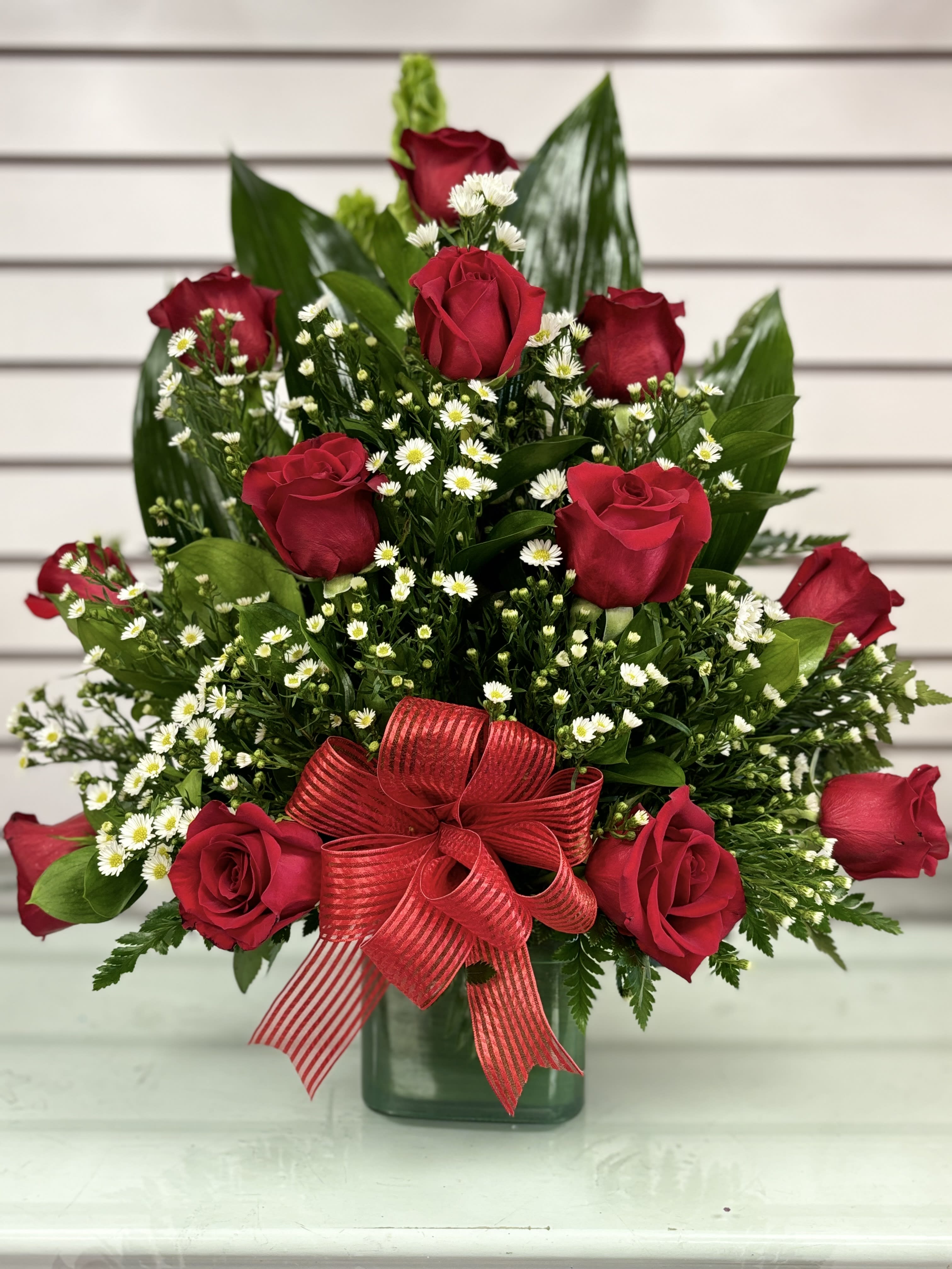 Red roses with white daisies in a green vase and red ribbon