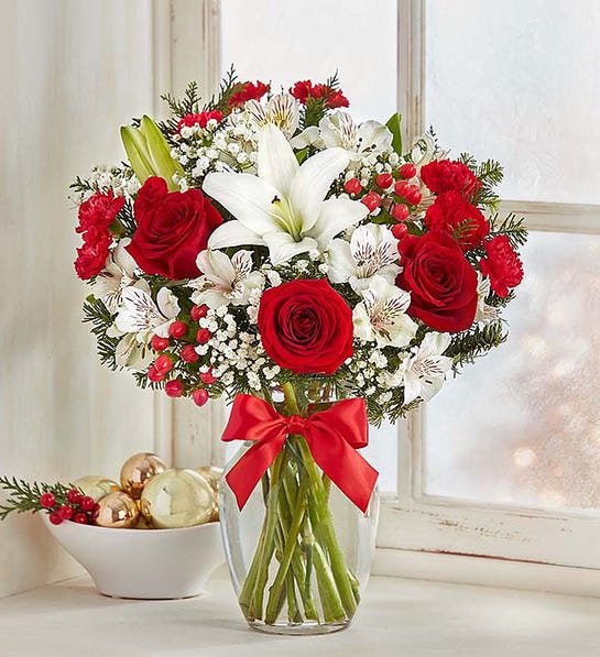 Red roses and white lilies in a clear glass vase with a red ribbon