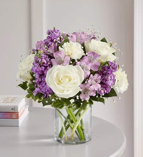 Bouquet of white roses and purple flowers in a clear glass vase