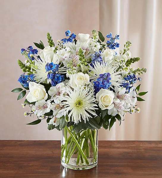 Sincerest Sorrow - Blue and White - Product ID: 95410   Beautiful in blue and white, our abundant sympathy arrangement makes a fitting remembrance during difficult times. Elegant roses, snapdragons, delphinium, stock, alstroemeria, spider mums and more are tastefully arranged by our florists in a classic glass vase. Lush blue and white arrangement of roses, snapdragons, delphinium, stock, alstroemeria, spider mums and monte casino, accented with variegated pittosporum and ruscus Hand-designed by our select florists in a classic glass cylinder vase; vase measures 8"H Can be sent to the home of friends, family members or business associates, or to the funeral service Large arrangement measures approximately 24"H x 22"L Medium arrangement measures approximately 22"H x 20"L Small arrangement measures approximately 20"H x 18"L Our florists hand-design each arrangement, so colors, varieties, and container may vary due to local availability