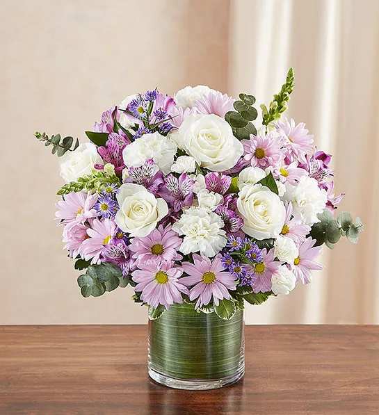 Cherished Memories - Lavender and White - Product ID: 95421   Remember a loved one with elegance and grace by sending our peaceful lavender and white arrangement in a classic cylinder vase. The freshest roses, snapdragons, alstroemeria, carnations and more are gathered by our florists to offer a tribute to a beautiful life. Graceful lavender and white arrangement of roses, snapdragons, alstroemeria, carnations, daisy poms, mini carnations and monte casino, gathered with variegated pittosporum and spiral eucalyptus Hand-designed by our expert florists in a stylish clear glass cylinder vase wrapped with a Ti leaf ribbon; vase measures 6"H Appropriate for the service or the home of friends and family members Large arrangement measures approximately 16"H x 17"L Medium arrangement measures approximately 15"H x 16"L Small arrangement measures approximately 14"H X 15"L Our florists hand-design each arrangement, so colors, varieties, and vase may vary due to local availability