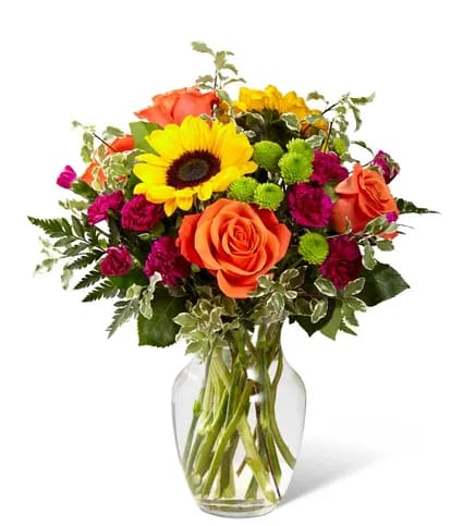 Bouquet of orange roses, yellow sunflowers, and magenta flowers in a glass vase